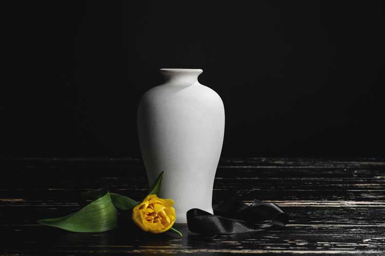 Mortuary urn with ribbon and flower on table against dark background